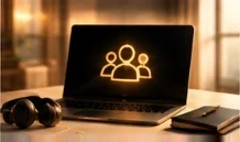 An open laptop glowing with a gold icon of three people, beside headphones and a notebook