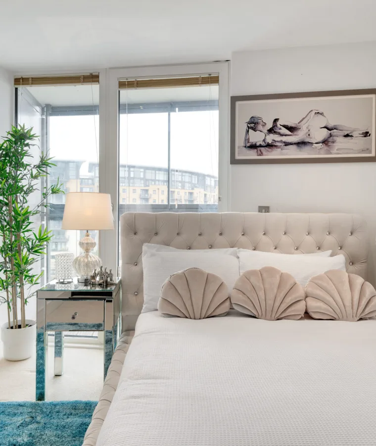 A Marlex bedroom with a tufted cream bed, shell cushions and a mirrored bedside table