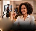 A smiling woman filming on her phone beside a phone on a small tripod