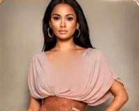 A woman with long dark hair and gold hoop earrings in a blush wrap top