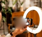 A hand holding a phone in a ring light, filming a woman for a skincare brand
