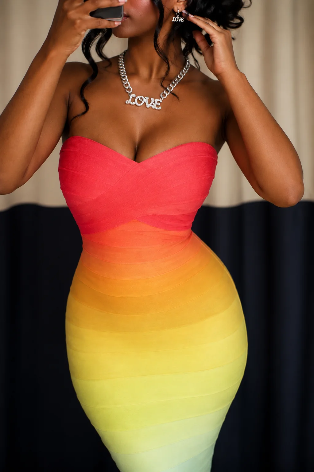 A strapless bandage dress shading from coral to yellow, with a LOVE necklace