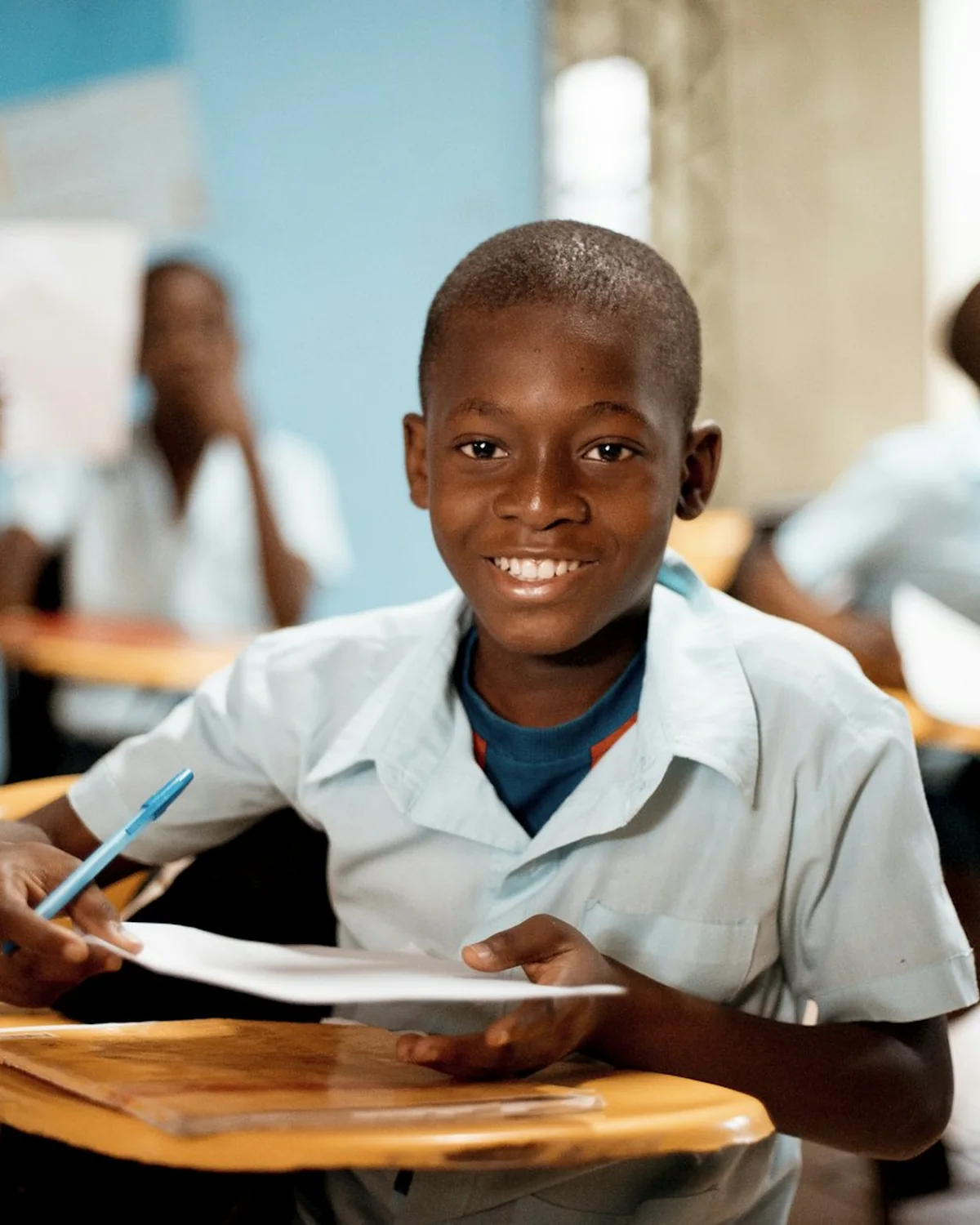 A boy at a school desk with a pen over his book